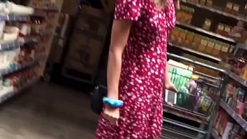 Under the skirt of a young sexy blonde wearing a red dress walking in a supermarket